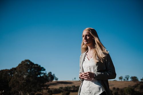 A blond haired adult female in the outback staring off into the distance