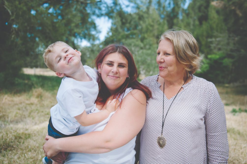 Two female adults, one is holding a male child all appear happy