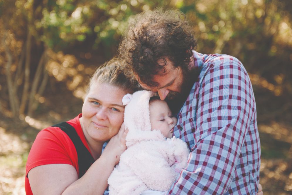 Two adults male and female holding an infant baby and cuddling it together smiling